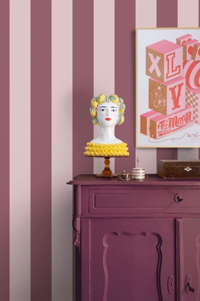 Vertikal gestreifte Tapete in Rosa und Burgunderrot hinter einer Kommode mit einer dekorativen Büste und einem gerahmten Bild.