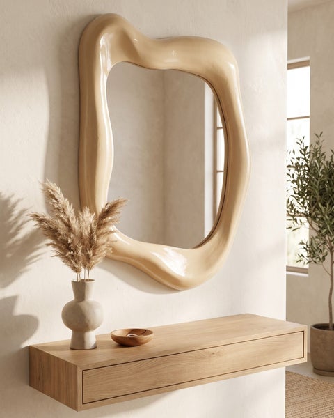 Wandspiegel mit unregelmaessigem, organisch geformtem Rahmen ueber einer hölzernen Wandkonsole mit Vase und Dekoschale im Wohnbereich.