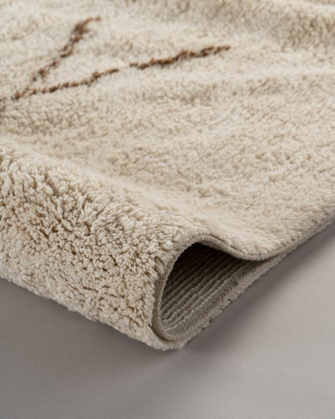 Nahaufnahme eines Hochflor-Teppichs mit weicher, zotteliger Struktur und geometrischem Muster.