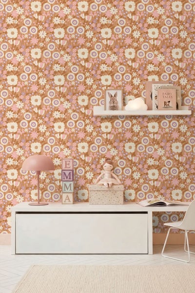 Kinderzimmer mit Blumenmuster-Tapete in Terrakotta und Rosa. Weißer Unterschrank, Wandregal mit Dekoration und eine rosa Tischlampe.