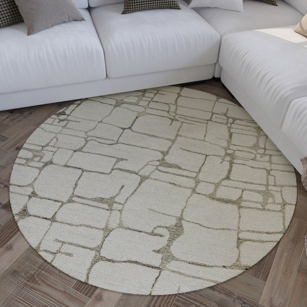 Runder Teppich mit abstraktem geometrischem Muster auf einem Holzfußboden in einem hellen Wohnzimmer vor einem Sofa.