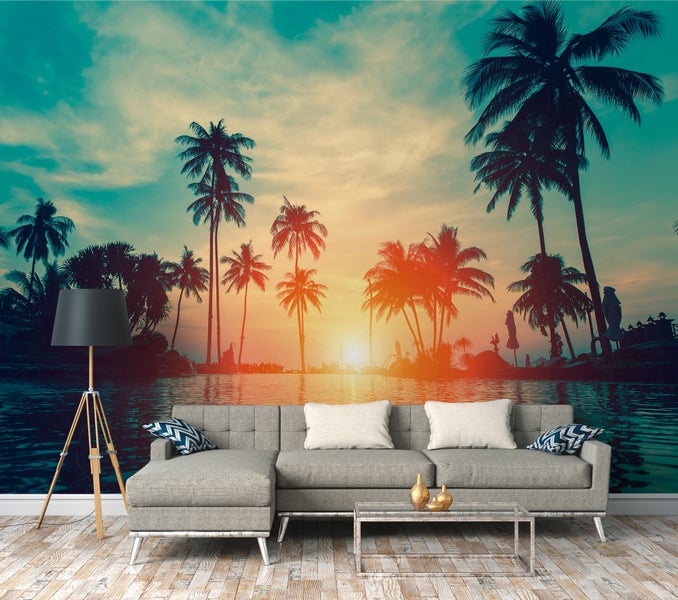 Fototapete mit tropischem Sonnenuntergang und Palmensilhouetten über Wasser in einem modernen Wohnzimmer mit grauem Sofa und Stehlampe.