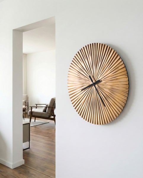 Goldene Wanduhr mit Strahlenmuster an einer weißen Wand