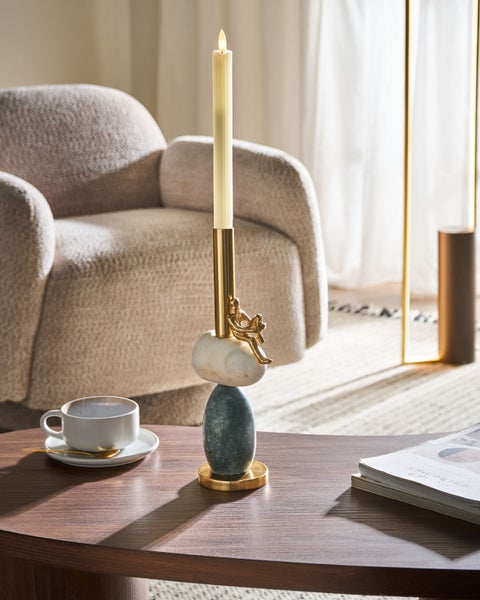 Dekoratives Wohnzimmer mit Kerzenständer, Sessel und Zeitschriften auf einem Couchtisch.