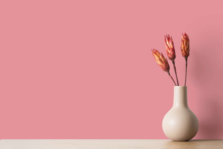 Beige Keramikvase mit drei Trockenblumen auf einer Holzoberfläche.