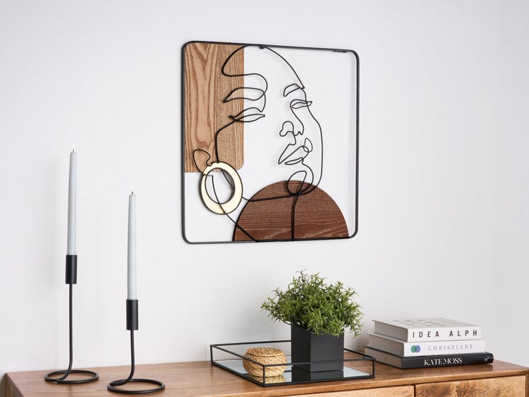 Moderne Wanddekoration aus schwarzem Metall mit abstraktem Gesicht, Holzelementen und goldenem Detail über einer Anrichte.
