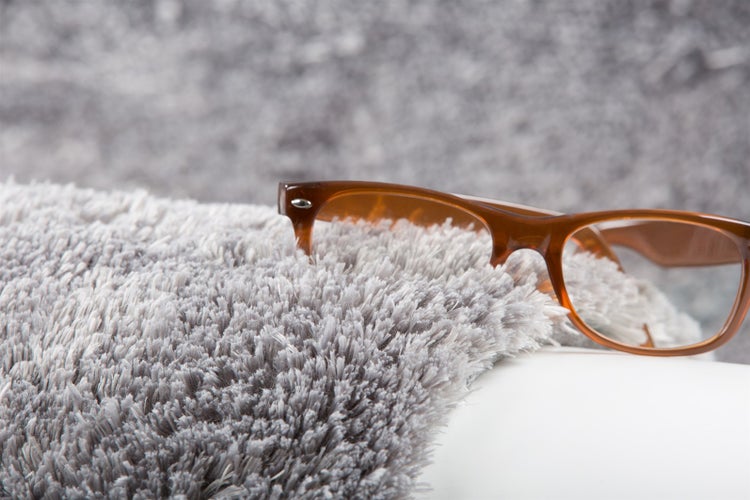 Nahaufnahme eines grauen Hochflor-Teppichs mit einer Brille zur Veranschaulichung der Florhöhe.