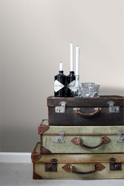 Dekorative Szene mit Vintage Koffern, Kerzen und Getränkeflaschen vor einer strukturierten Wand