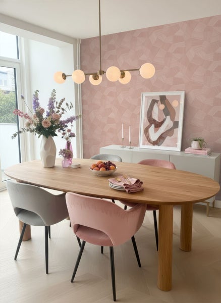 Modernes Esszimmer mit rosa geometrischer Tapete, ovalem Holztisch, Samtstühlen in Rosa und Grau sowie einer Pendelleuchte mit Glaskugeln.