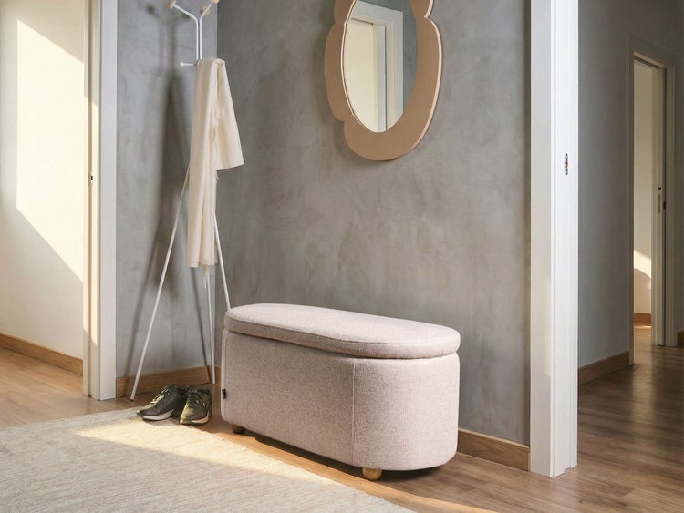 Gepolsterte Sitzbank mit Stauraum in einem hellen Flur vor einer grauen Wand mit Spiegel und Garderobe.