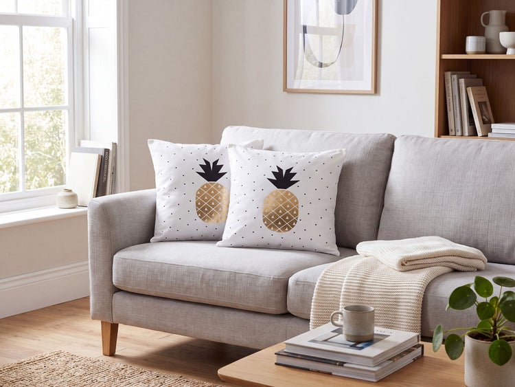 Zwei quadratische Sofakissen mit Ananasmuster auf einem hellgrauen Sofa in einem modernen Wohnzimmer