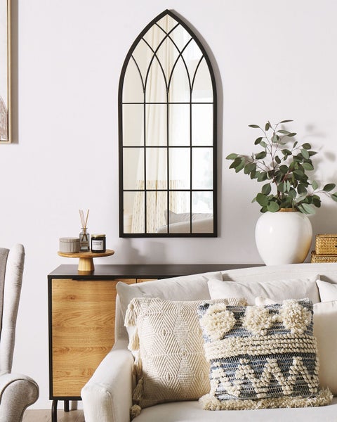 Dekoratives Zimmer mit einem Spiegel im gotischen Stil, einer Kommode und Kissen auf dem Sofa.