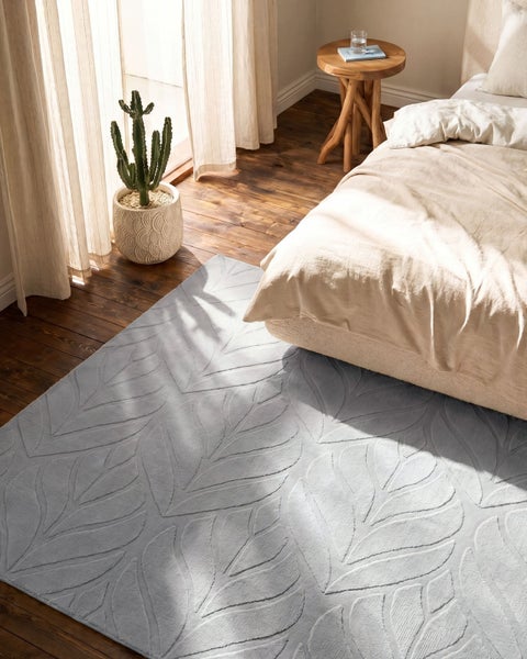 Hellblauer Teppich mit Blattmuster auf Holzboden in einem hellen Schlafzimmer neben einem Bett.
