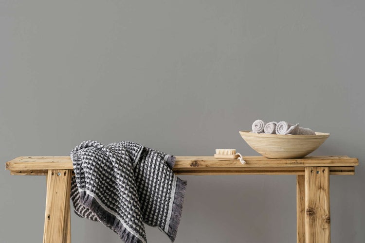 Rustikale Holzbank mit gemustertem Handtuch, kleiner Holzbürste und einer Holzschale mit gerollten Gästehandtüchern.