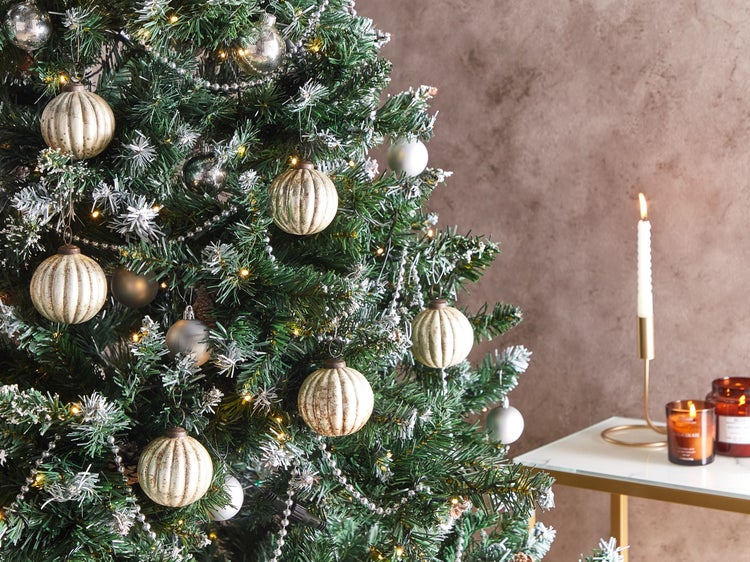 Dekorierter Weihnachtsbaum mit Kugeln und Lichterkette, Tisch mit Kerzenleuchter und Duftkerzen