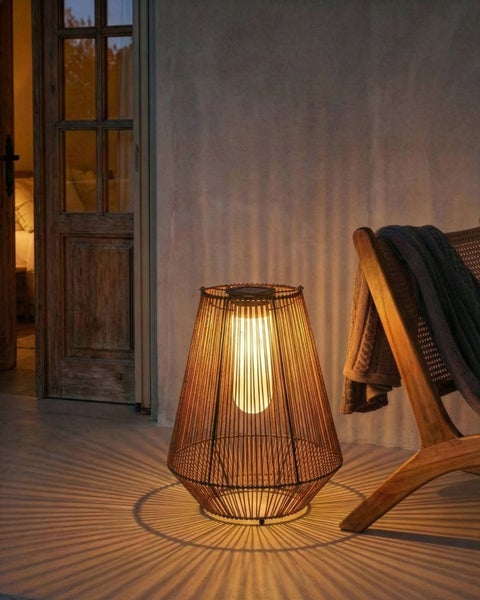Solar-Bodenleuchte in Kegelform aus feinen Holzstreben, strahlt warmweißes Licht aus und wirft ein dekoratives Schattenmuster auf den Boden.