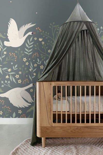 Kinderzimmer mit hölzernem Kinderbett und Baldachin vor einer Tapete mit Schwanenmotiven