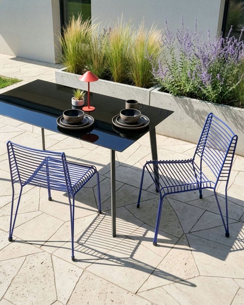Esstisch mit Glasplatte und zwei Metallstühlen im Freien