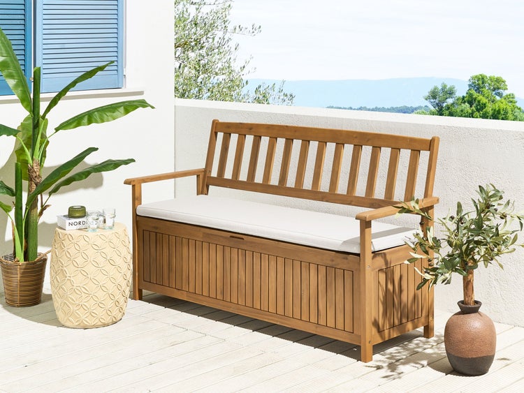 Gartenbank aus Holz mit integriertem Stauraum und hellem Sitzkissen auf einer hellen Terrasse mit Pflanzen.