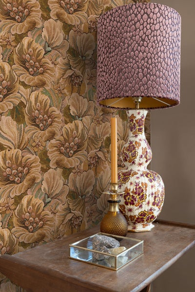 Dekorative Szene mit Lampe, Kerze und kleinem Behälter auf einem Tisch vor einer gemusterten Tapete