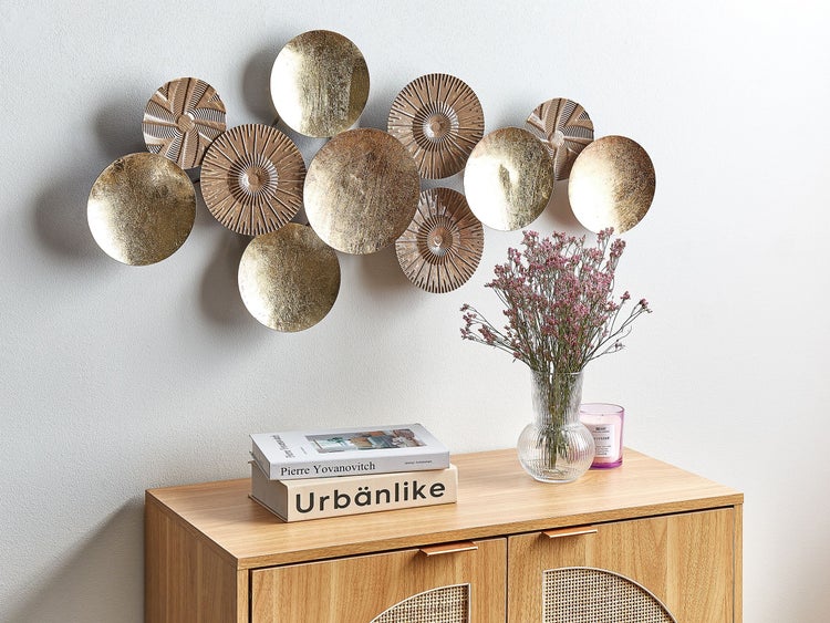 Wohnraum mit goldfarbener Wanddekoration aus Metall, Kommode, Blumenvase und Kerze