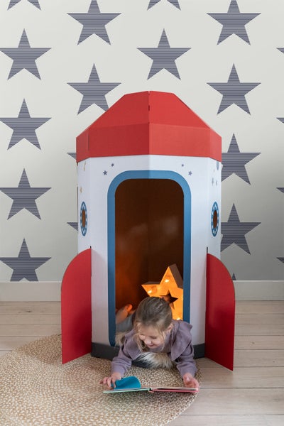 Mädchen liest in einem Raketen-Spielhaus aus Karton auf einem Teppich