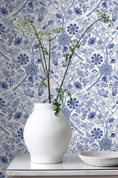 Helle, organisierte Szene mit klassischer Vliestapete im blauen Blumenmuster, weiße Vase mit Zweigen und Schale im Vordergrund.