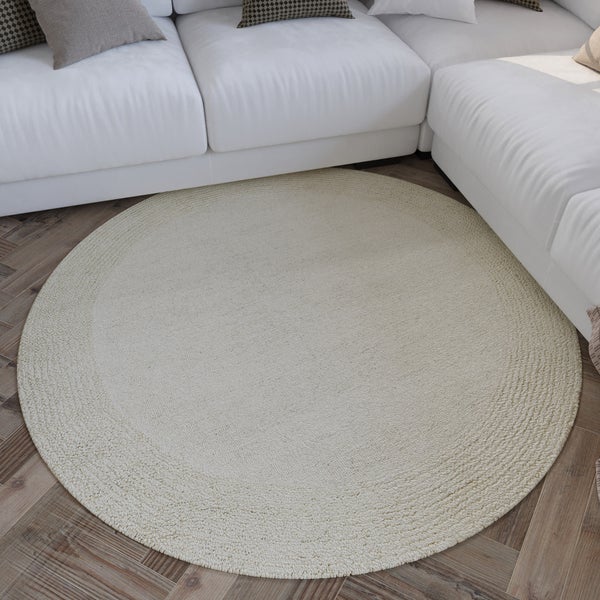Runder, strukturierter Teppich in einem modernen Wohnzimmer auf Holzparkett im Fischgrätmuster vor einem weißen Sofa.