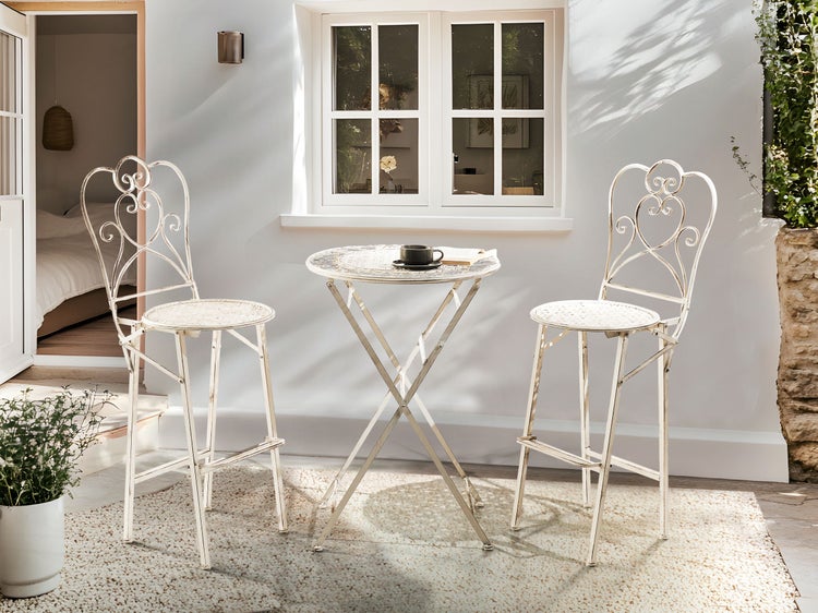 Gartenszene mit Bistrotisch und zwei Stühlen im Freien.