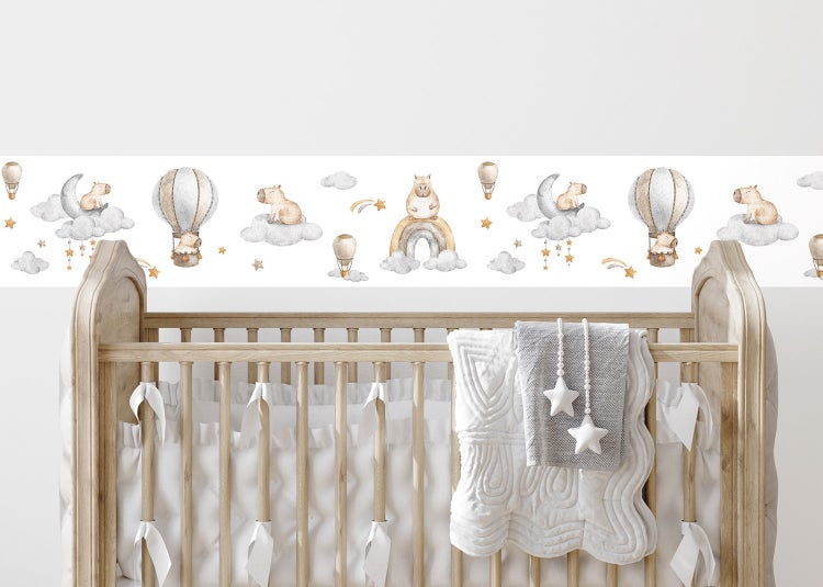 Selbstklebende Tapetenbordüre für Kinderzimmer mit Tiermotiven, Heißluftballons und Regenbögen im Aquarell-Stil, angebracht über einem Bett.