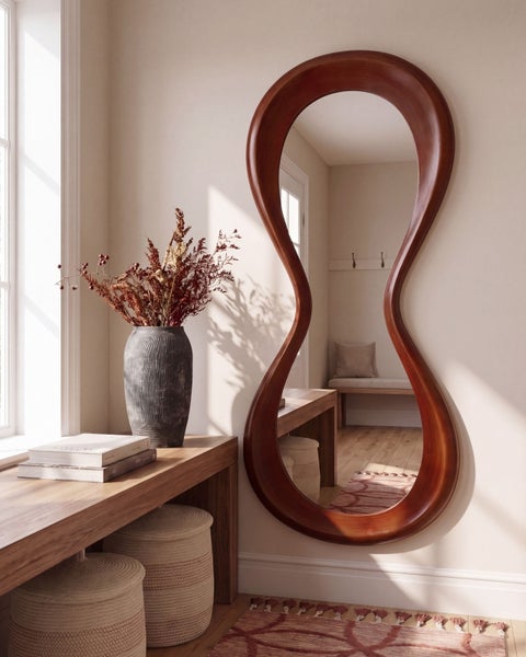 Ein organischer Wandspiegel mit dunklem Holzrahmen hängt über einer hölzernen Konsole mit einer Vase und dekorativen Objekten im Flurbereich.
