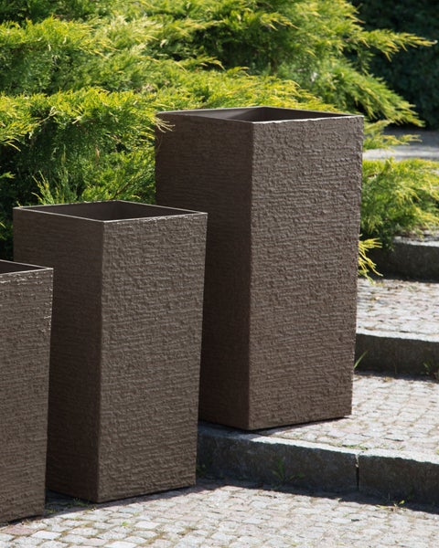 Drei Pflanzkübel aus Kunststein im Garten.