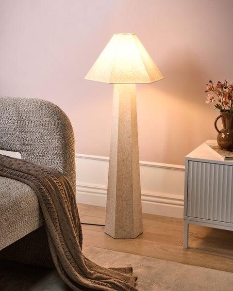 Beleuchtete Stehlampe neben Sessel und Kommode in einem Zimmer