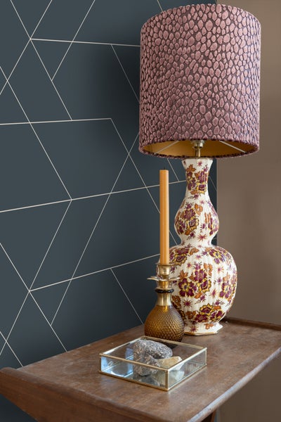 Dekoratives Interieur mit Lampe, Kerze und geometrischer Tapete auf einem Holztisch