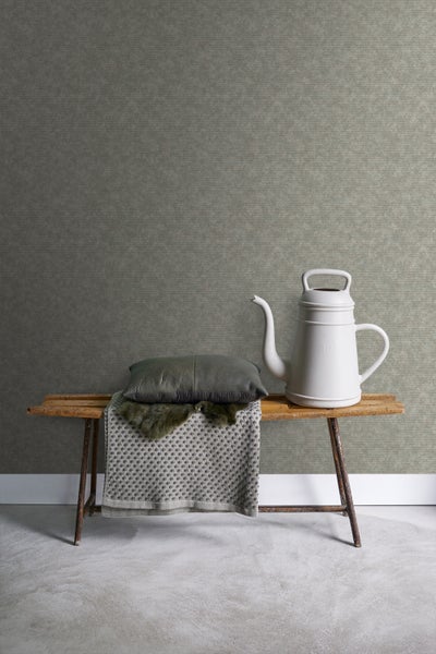 Dekoratives Interieur mit Bank, Kissen, Decke und Gießkanne vor einer strukturierten Tapete