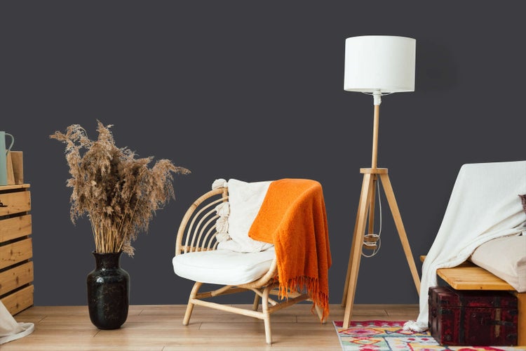 Dunkelgrau gestrichene Wand in einem Wohnzimmer mit Rattansessel, Stativ-Stehleuchte und Trockenblumen.