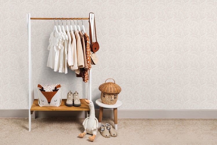 Dekorative Kinderzimmergestaltung mit Kleiderständer, Spielzeug und Accessoires vor einer gemusterten Tapete.