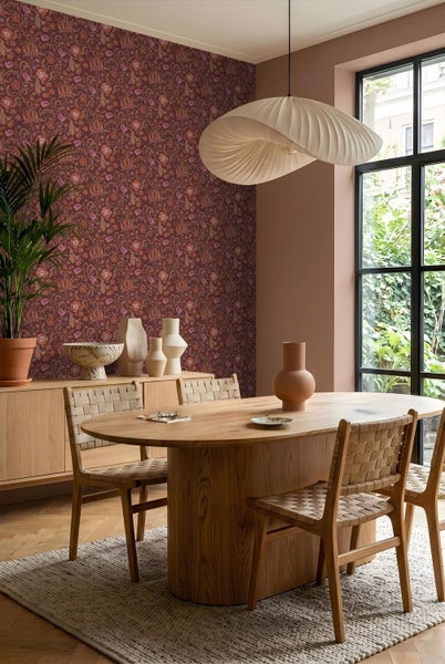 Modernes Esszimmer mit roter Blumentapete, ovalem Holztisch, geflochtenen Stühlen und einer großen plissierten Pendelleuchte.