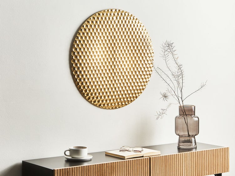 Dekorative Szene mit einem goldenen Wandobjekt, einer Kommode, einer Vase und verschiedenen Deko-Artikeln