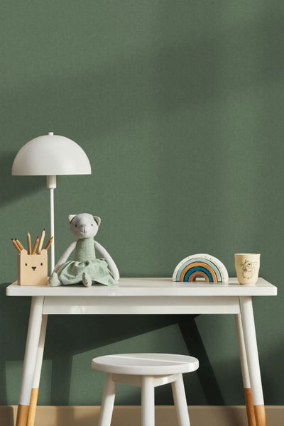 Dunkelgrüne Tapete in Textiloptik hinter einem weißen Kinderschreibtisch mit Schreibtischlampe, Holzspielzeug und Stofftier.