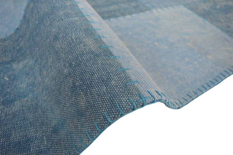 Blaue Patchwork-Teppich-Nahaufnahme mit sichtbaren Ziernähten und feiner Webstruktur.