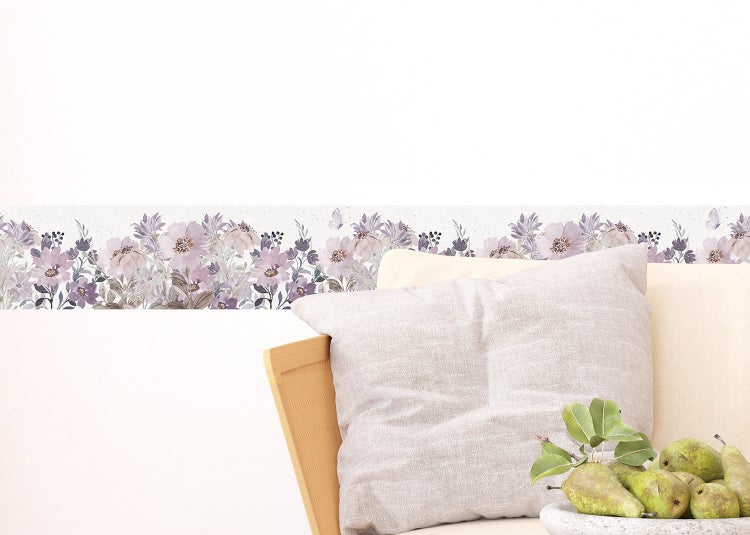 Tapetenbordüre mit lila Blumenmuster im Aquarellstil neben einem Sofa mit Kissen und einer Schale Birnen.