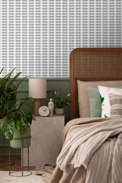 Schlafzimmer mit Bett, Nachttisch, Lampe und Zimmerpflanzen vor einer Wand mit floraler Tapete.