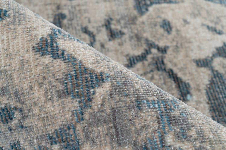 Detailaufnahme eines gewebten Teppichs in Beige und Blau mit Vintage-Muster und sichtbarer Struktur.