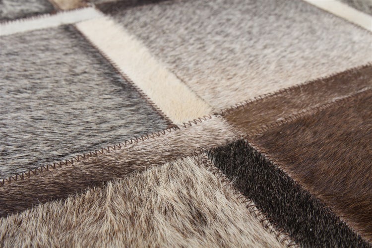 Detailansicht eines Patchwork-Teppichs aus echtem Kuhfell mit sichtbaren Zickzack-Nähten in verschiedenen Braun- und Grautönen.