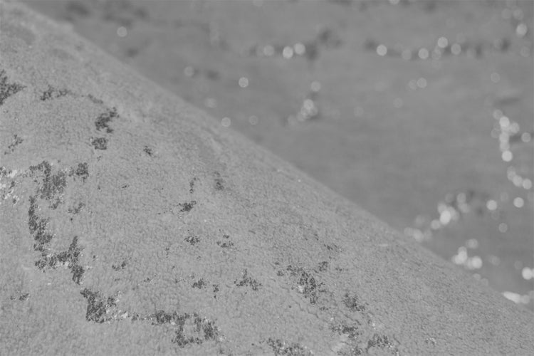 Nahaufnahme einer strukturierten Natursteinoberfläche mit abgerundeter Kante und sichtbarer Maserung.