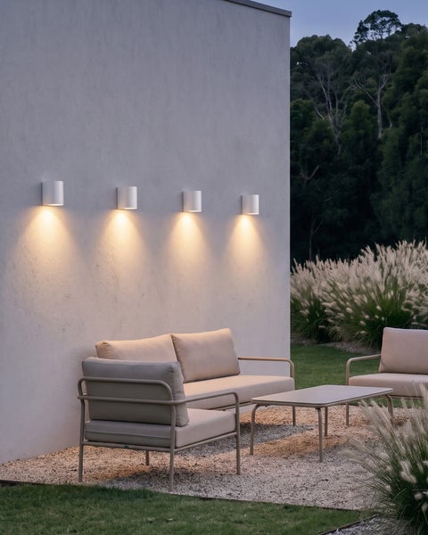 Vier moderne, zylindrische Außenwandleuchten beleuchten eine gemütliche Sitzecke auf der Terrasse im Garten.