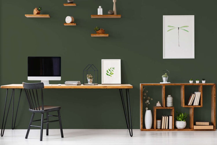 Modernes Heimbüro mit dunkelgrüner Wand, Schreibtisch aus Holz, schwarzem Stuhl und einem offenen Holzregal für Dekoration und Bücher.