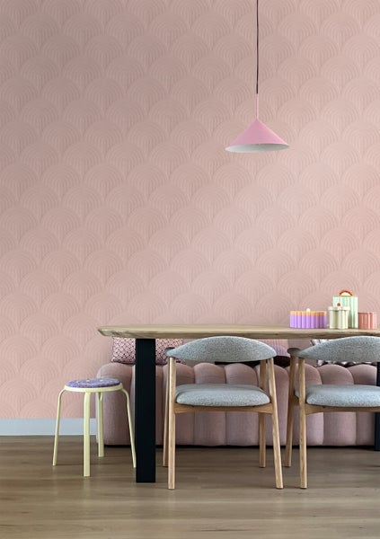 Rosa Zimmer mit Esstisch, Stühlen, Hocker und Pendelleuchte vor gemusterter Tapete.