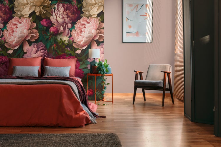 Modernes Schlafzimmer mit großflächiger Blumentapete, rotem Bett, einem grauen Sessel und Parkettboden.